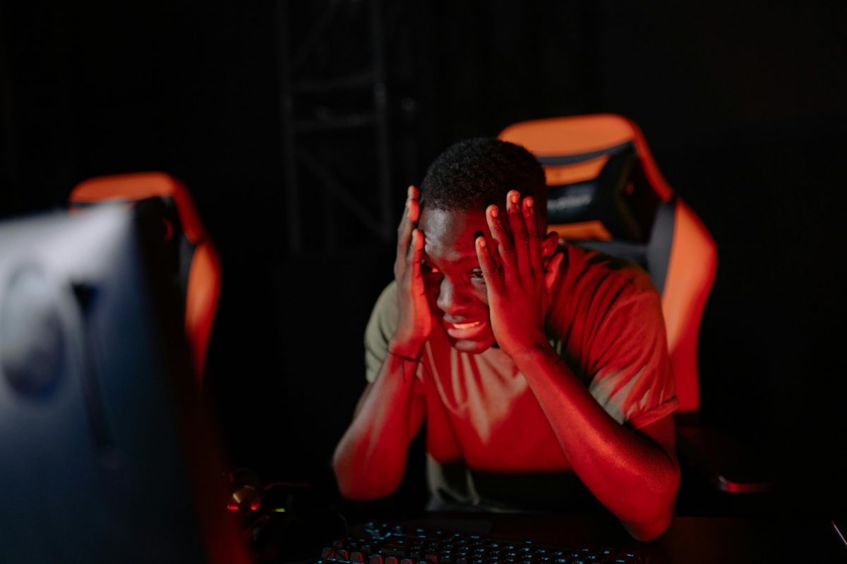 A man intensely reacts to a game loss at his computer in a dimly lit gaming room.